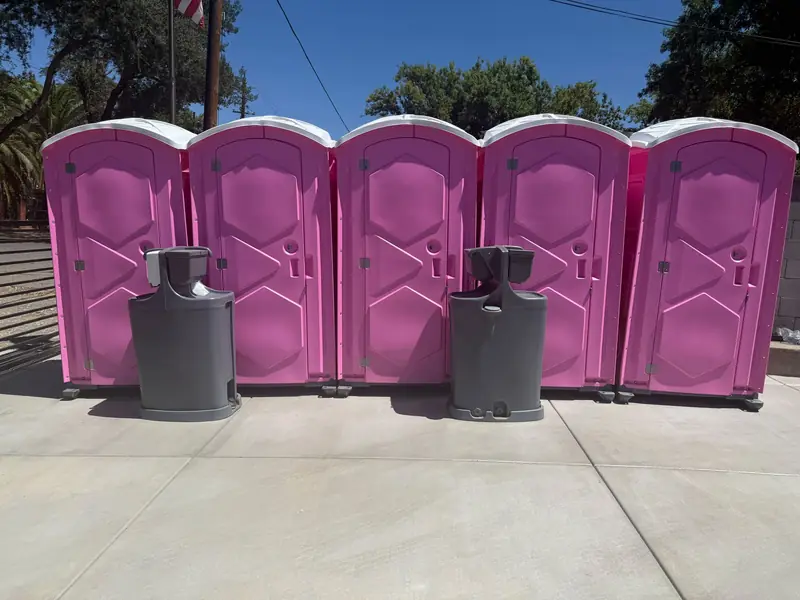 Row of pink event portable toilets with freestanding hand-wash stations between them