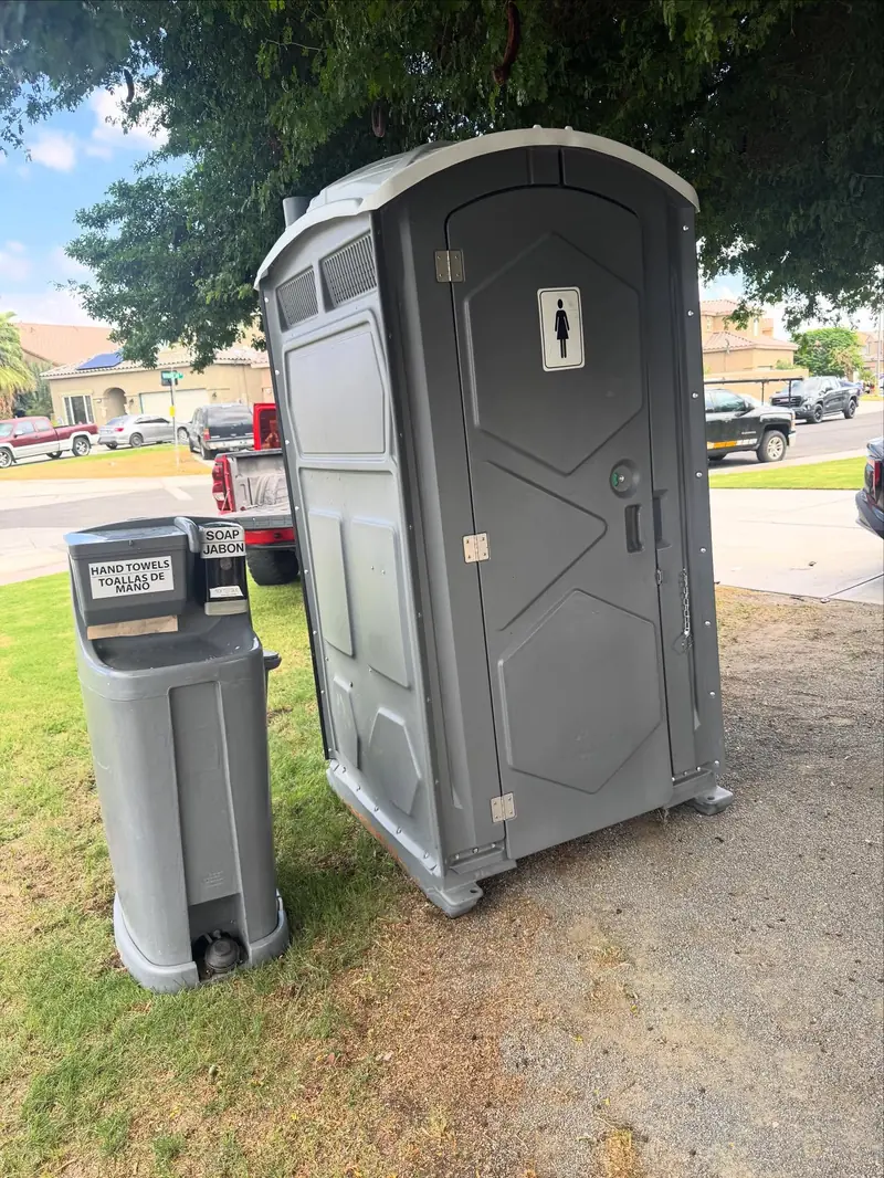 Grey portable toilet with a freestanding hand-wash station set up on a lawn